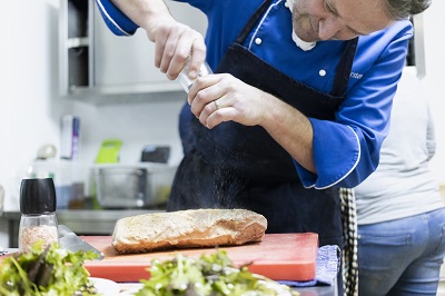 Mann im Kochkurs würzt ein Stück Fleisch